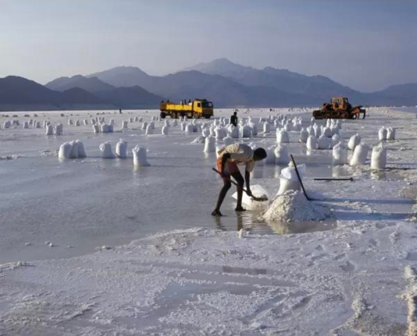 Wide view of salt harvesting on the Lac Assal flat with mountains and trucks in background